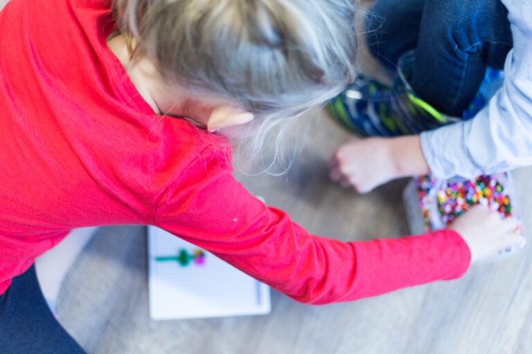 Twee kinderen spelen met kralen op de vloer