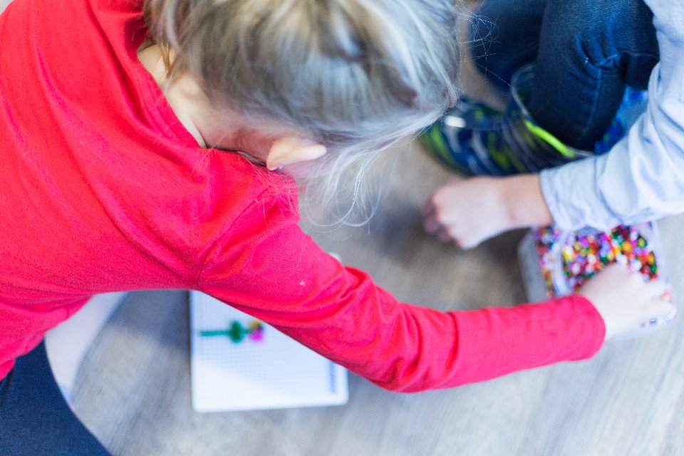 Twee kinderen spelen met kralen op de vloer